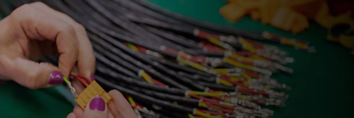 An image of a hand connecting electrical wires to a yellow hub against a background of a pile of additional wires.